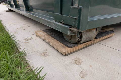 Plywood and matting protecting a driveway under a dumpster rail
